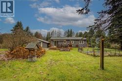 Rear view of house with a wooden deck, a yard, a vegetable garden, and view of scattered trees - 