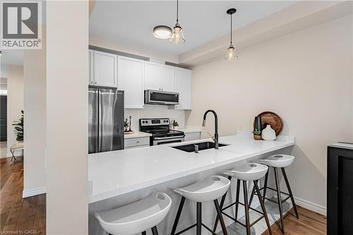 Kitchen with a breakfast bar area, appliances with stainless steel finishes, white cabinetry, dark wood finished floors, and a peninsula - 5056 New Street Unit# 21, Burlington, ON - Indoor Photo Showing Kitchen With Stainless Steel Kitchen