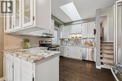 Kitchen featuring white cabinets, light stone counters, stainless steel appliances, and backsplash - 