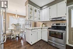 Kitchen featuring appliances with stainless steel finishes, white cabinets, glass insert cabinets, tasteful backsplash, and light stone counters - 