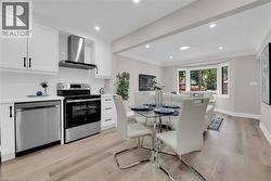 Kitchen featuring white cabinets, stainless steel appliances, wall chimney range hood, recessed lighting, and light wood finished floors - 