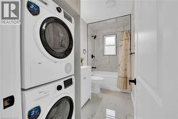 Bathroom with light marble finish flooring, vanity, a combined bath / shower with marble appearance, and stacked washer / dryer - 
