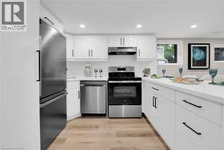 Kitchen featuring appliances with stainless steel finishes, white cabinetry, light wood-style flooring, recessed lighting, and under cabinet range hood - 