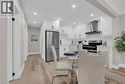Kitchen featuring white cabinetry, stainless steel appliances, light countertops, wall chimney exhaust hood, and recessed lighting - 