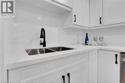 Kitchen featuring white cabinets, decorative backsplash, light stone countertops, and dishwasher - 
