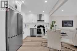 Kitchen featuring stainless steel appliances, white cabinets, light wood-type flooring, wall chimney range hood, and open floor plan - 