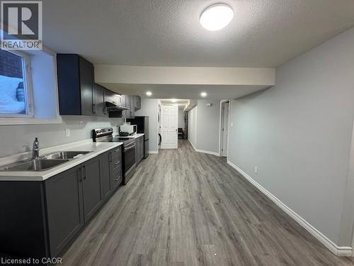 Kitchen featuring electric stove, light countertops, light wood-style floors, a textured ceiling, and under cabinet range hood - 509 St Moritz Avenue Unit# Lower, Waterloo, ON - Indoor Photo Showing Kitchen With Double Sink