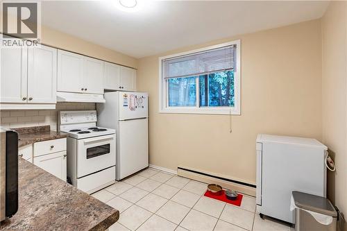 Kitchen featuring white appliances, dark countertops, white cabinets, and baseboard heating - 62 Moore Avenue, Kitchener, ON - Indoor Photo Showing Kitchen