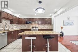 Kitchen featuring dark brown cabinetry, a breakfast bar, appliances with stainless steel finishes, light stone counters, and pendant lighting - 