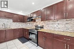 Kitchen featuring stainless steel range with electric cooktop, light stone countertops, dark brown cabinets, under cabinet range hood, and light tile patterned floors - 