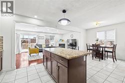 Kitchen with dark brown cabinetry, open floor plan, light stone countertops, a fireplace, and decorative light fixtures - 