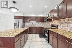 Kitchen featuring range with electric stovetop, light stone counters, stainless steel fridge with ice dispenser, dark brown cabinetry, and under cabinet range hood - 