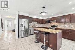 Kitchen with dark brown cabinets, a kitchen bar, appliances with stainless steel finishes, pendant lighting, and light stone countertops - 