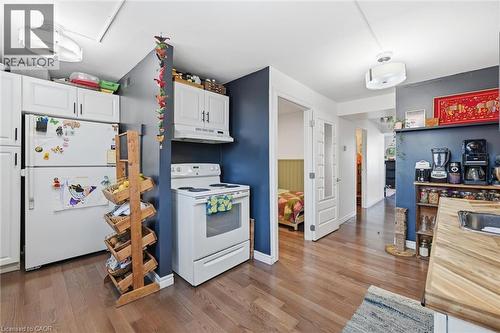 Kitchen with white appliances, white cabinets, dark wood-style floors, and under cabinet range hood - 18 Fraser Avenue, Hamilton, ON - Indoor Photo Showing Kitchen