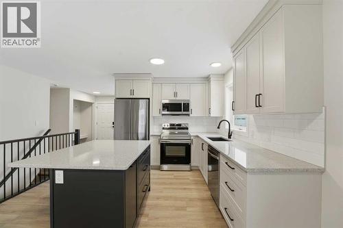 The stunning kitchen showcases ceiling-height cream cabinetry, quartz countertops, a subway tile backsplash, an upgraded stainless steel appliance package, and a contrasting island with dark cabinetry - 82 Bruns Crescent, Lacombe, AB - Indoor Photo Showing Kitchen With Stainless Steel Kitchen With Upgraded Kitchen