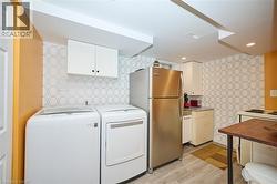 Washroom featuring wallpapered walls, washer and clothes dryer, light wood-style flooring, and recessed lighting - 