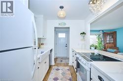 Kitchen featuring white appliances, white cabinetry, light stone counters, and pendant lighting - 
