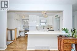 Kitchen featuring white cabinetry, white appliances, light wood-style flooring, decorative backsplash, and a peninsula - 