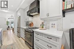 Kitchen featuring appliances with stainless steel finishes, custom range hood, white cabinets, and light wood-type flooring - 