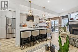 Kitchen with decorative light fixtures, light wood-type flooring, stainless steel refrigerator with ice dispenser, a kitchen bar, and a center island with sink - 