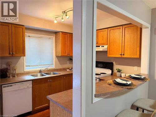 Kitchen featuring white appliances, a breakfast bar, under cabinet range hood, brown cabinetry, and light countertops - 2258 Empire Crescent, Burlington, ON - Indoor Photo Showing Kitchen With Double Sink