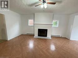 Unfurnished living room with a fireplace with flush hearth, parquet floors, a ceiling fan, baseboard heating, and a textured ceiling - 