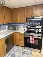 Kitchen with brown cabinetry, stainless steel appliances, under cabinet range hood, a paneled ceiling, and light tile patterned flooring - 