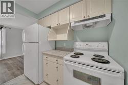 Kitchen featuring white appliances, under cabinet range hood, light countertops, white cabinets, and light marble finish flooring - 