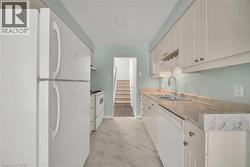 Kitchen with white appliances, light countertops, white cabinetry, and light marble finish floors - 