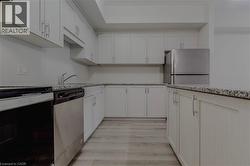 Kitchen with light stone counters, light wood-style flooring, white cabinetry, appliances with stainless steel finishes, and a sink - 