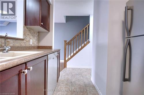 Kitchen with freestanding refrigerator, dishwasher, light tile patterned floors, tasteful backsplash, and light stone counters - 919 Zeller Crescent, Kitchener, ON - Indoor