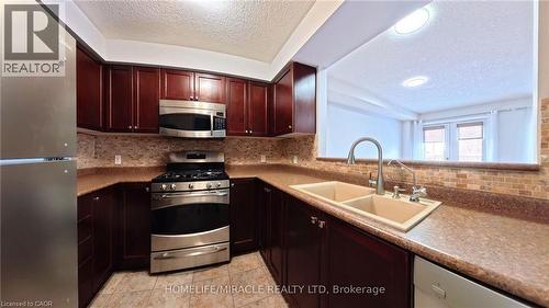 Kitchen with appliances with stainless steel finishes, a textured ceiling, decorative backsplash, reddish brown cabinets, and light tile patterned floors - 919 Zeller Crescent, Kitchener, ON - Indoor Photo Showing Kitchen With Double Sink