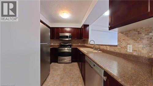 Kitchen featuring appliances with stainless steel finishes, a textured ceiling, backsplash, dark countertops, and light tile patterned floors - 919 Zeller Crescent, Kitchener, ON - Indoor Photo Showing Kitchen With Double Sink