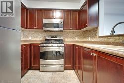 Kitchen with stainless steel appliances, reddish brown cabinets, light tile patterned floors, and decorative backsplash - 