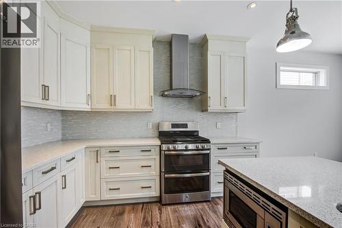 Kitchen featuring stainless steel appliances, wall chimney exhaust hood, decorative backsplash, light stone counters, and pendant lighting - 2527 Holbrook Drive, London, ON - Indoor Photo Showing Kitchen