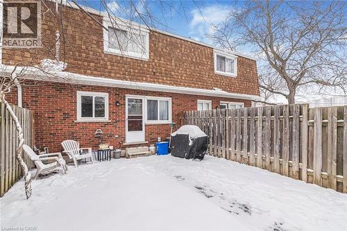 Snow covered back of property with mansard roof, a fenced backyard, roof with shingles, and brick siding - 48 Riverdale Drive Unit# 2, Hamilton, ON - Outdoor With Exterior
