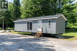 View of front of property featuring entry steps, view of wooded area, and roof with shingles - 