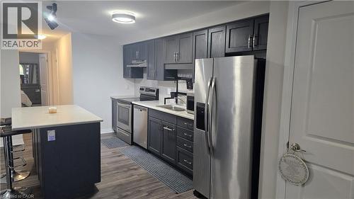 Kitchen featuring a kitchen breakfast bar, stainless steel appliances, dark wood finished floors, under cabinet range hood, and a kitchen island - 115 South Creek Drive Unit# 15D, Kitchener, ON - Indoor Photo Showing Kitchen