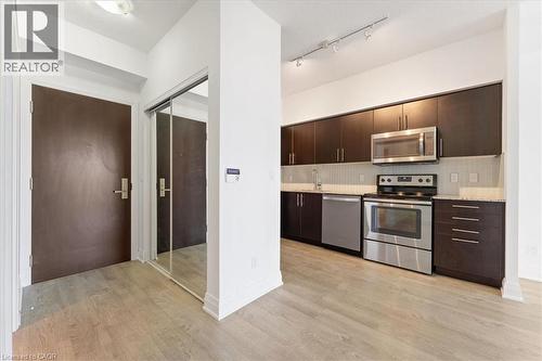 Kitchen with dark brown cabinets, appliances with stainless steel finishes, modern cabinets, light wood-style floors, and backsplash - 55 Speers Road Unit# 415, Oakville, ON - Indoor Photo Showing Kitchen With Stainless Steel Kitchen