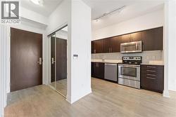 Kitchen with dark brown cabinets, appliances with stainless steel finishes, modern cabinets, light wood-style floors, and backsplash - 