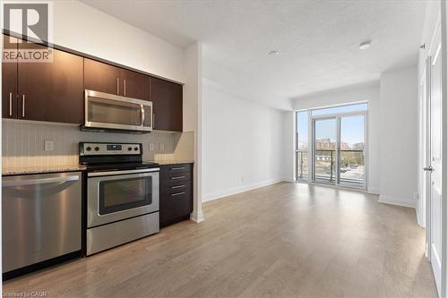 Kitchen featuring appliances with stainless steel finishes, dark brown cabinetry, light wood-style floors, backsplash, and a textured ceiling - 55 Speers Road Unit# 415, Oakville, ON - Indoor Photo Showing Kitchen With Stainless Steel Kitchen