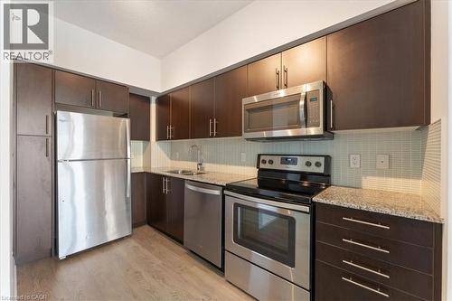 Kitchen featuring dark brown cabinets, stainless steel appliances, light wood-type flooring, and light stone counters - 55 Speers Road Unit# 415, Oakville, ON - Indoor Photo Showing Kitchen With Stainless Steel Kitchen With Double Sink