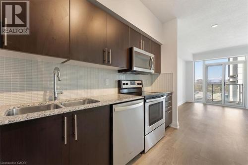 Kitchen featuring dark brown cabinets, stainless steel appliances, light wood-type flooring, and light stone countertops - 55 Speers Road Unit# 415, Oakville, ON - Indoor Photo Showing Kitchen With Stainless Steel Kitchen With Double Sink With Upgraded Kitchen