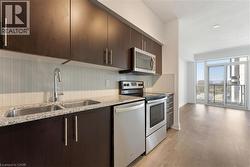 Kitchen featuring dark brown cabinets, stainless steel appliances, light wood-type flooring, and light stone countertops - 
