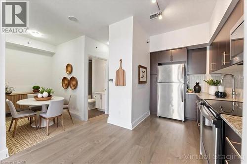 Kitchen featuring stainless steel appliances, light wood-style flooring, modern cabinets, backsplash, and light stone countertops - 55 Speers Road Unit# 415, Oakville, ON - Indoor
