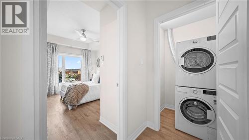 Washroom with light wood finished floors, stacked washer / dryer, and ceiling fan - 610 Farmstead Drive Unit# 304, Milton, ON - Indoor Photo Showing Laundry Room