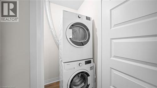 Washroom with stacked washer / drying machine and wood finished floors - 610 Farmstead Drive Unit# 304, Milton, ON - Indoor Photo Showing Laundry Room