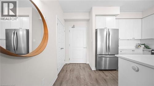 Kitchen featuring white cabinetry, freestanding refrigerator, light wood-style flooring, tasteful backsplash, and a textured ceiling - 610 Farmstead Drive Unit# 304, Milton, ON - Indoor Photo Showing Kitchen With Stainless Steel Kitchen