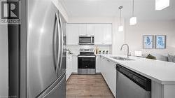 Kitchen with stainless steel appliances, white cabinets, light wood-type flooring, decorative light fixtures, and light stone countertops - 