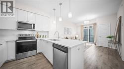 Kitchen with stainless steel appliances, tasteful backsplash, a peninsula, light wood-type flooring, and white cabinets - 